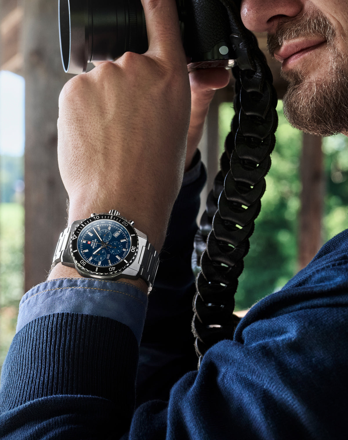 A close-up lifestyle shot of a man holding a camera, wearing the silver-toned Solar Power SMS34113.02  wristwatch with a blue dial and a black rotating bezel.